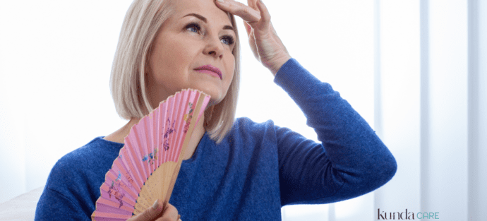 Mulher sentindo calor e abanando-se com um leque, representando ondas de calor comuns na menopausa.